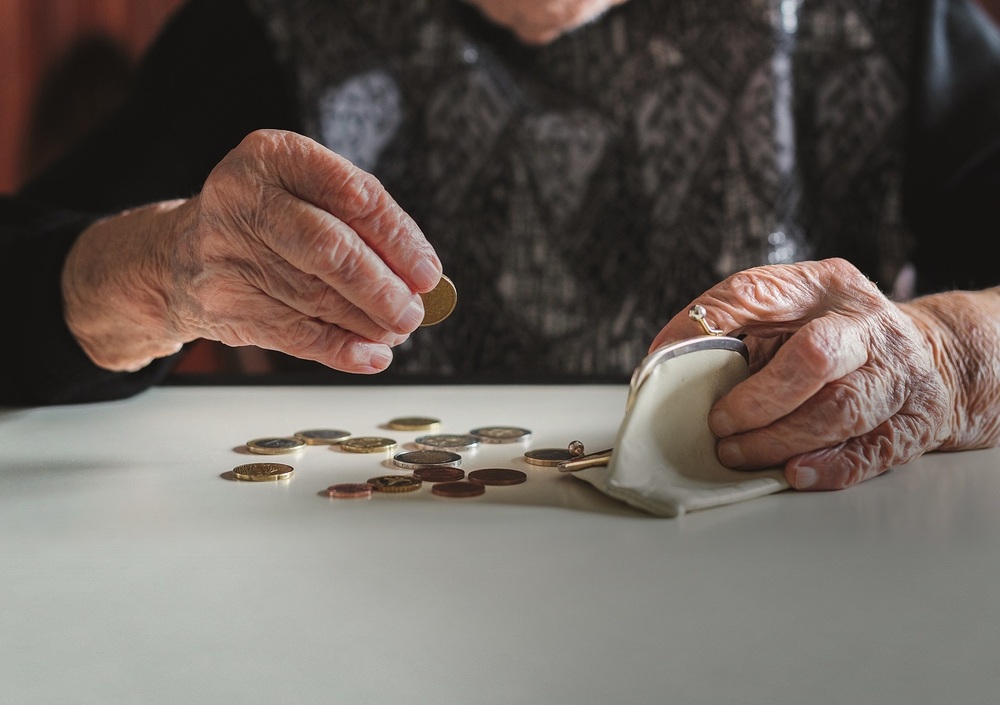 Elderly woman sitting at the table counting money in her wallet. / Matej Kastelic, kasto80 Elderly 95 years old woman sitting miserably at the table at home and counting remaining coins from the pension in her wallet after paying the bills.